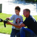 Devon Wallace of Osawatomie mans the fire hose with the help of Osawatomie fire fighter Rusty Thomas Saturday morning at the fire station's open house.